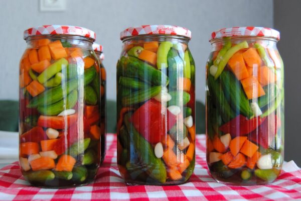 Three jars of assorted pickled vegetables on a red checkered tablecloth.